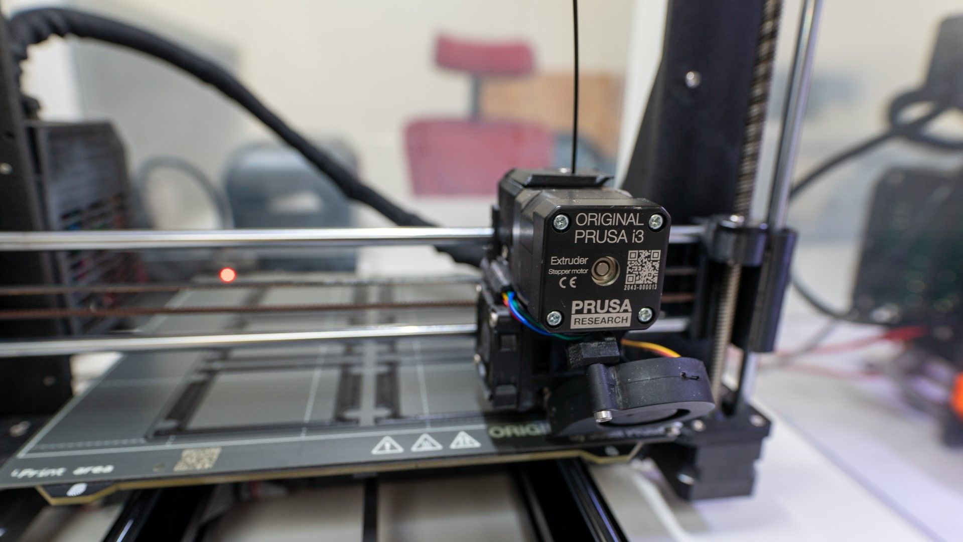 Close-up of a 3D printer's print head with the text 'ORIGINAL PRUSA i3 MK3S+' visible.