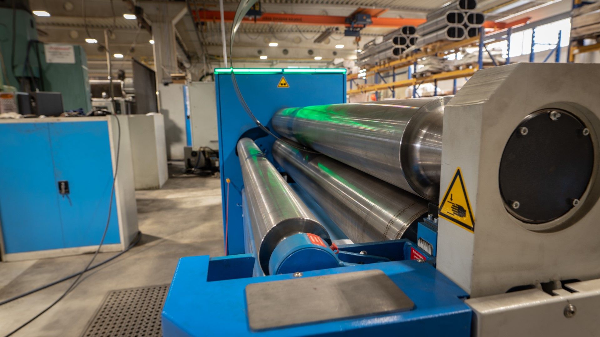 Industrial metal rolling machine with three large cylinders in a factory setting.