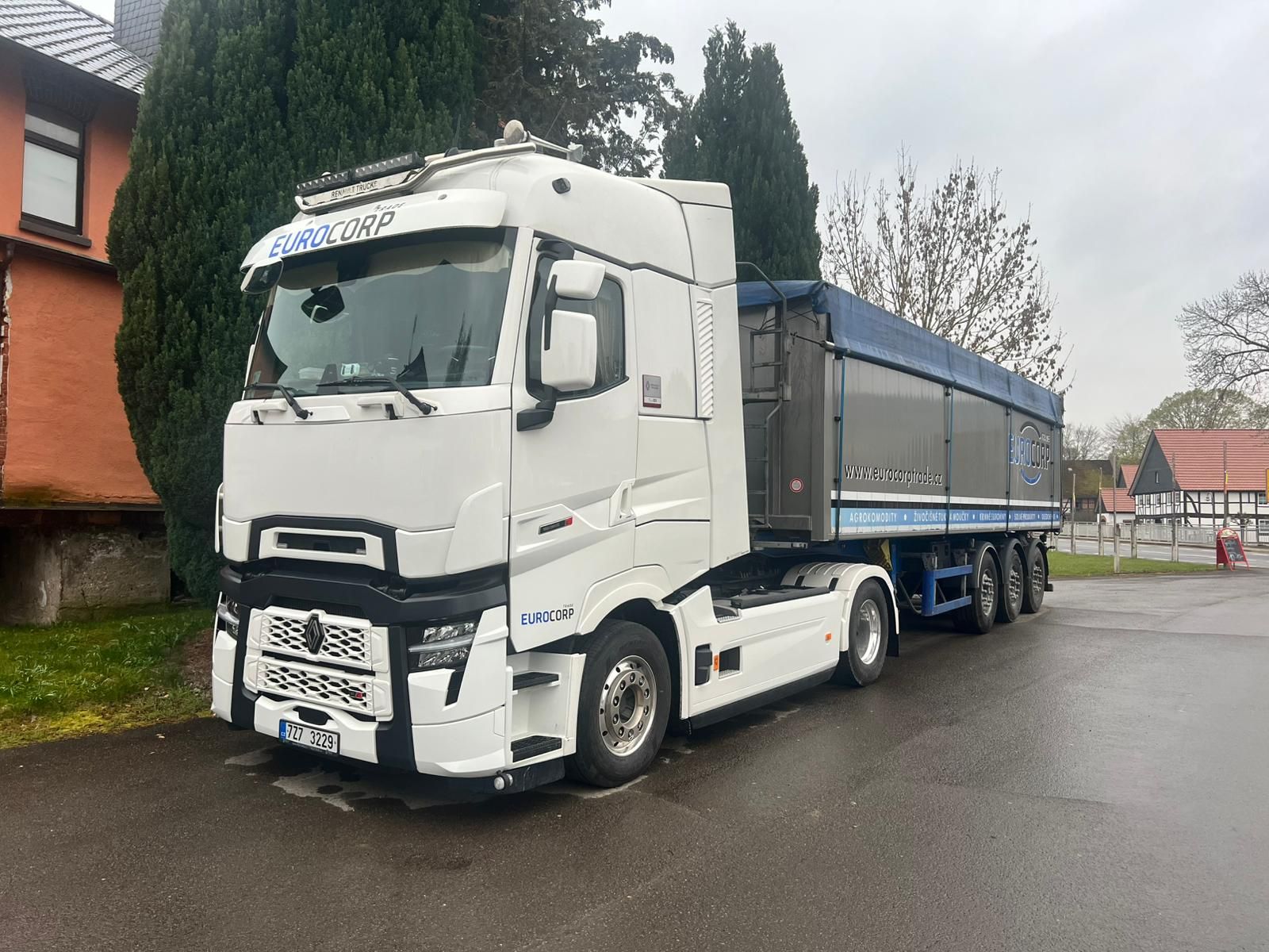 A white semi-truck with a blue cargo trailer parked on a paved road.