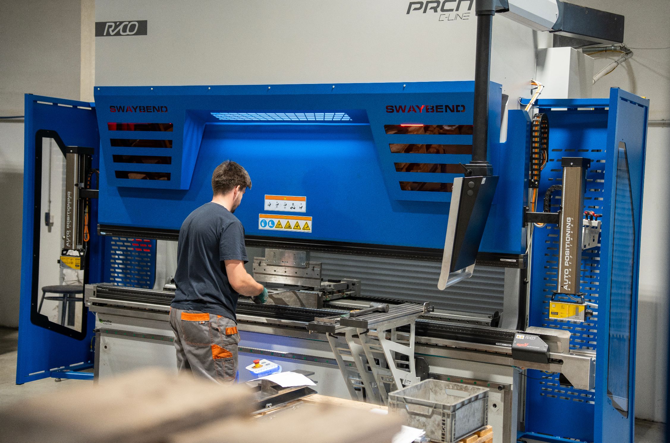 Man operating a large blue industrial press brake machine in a workshop.