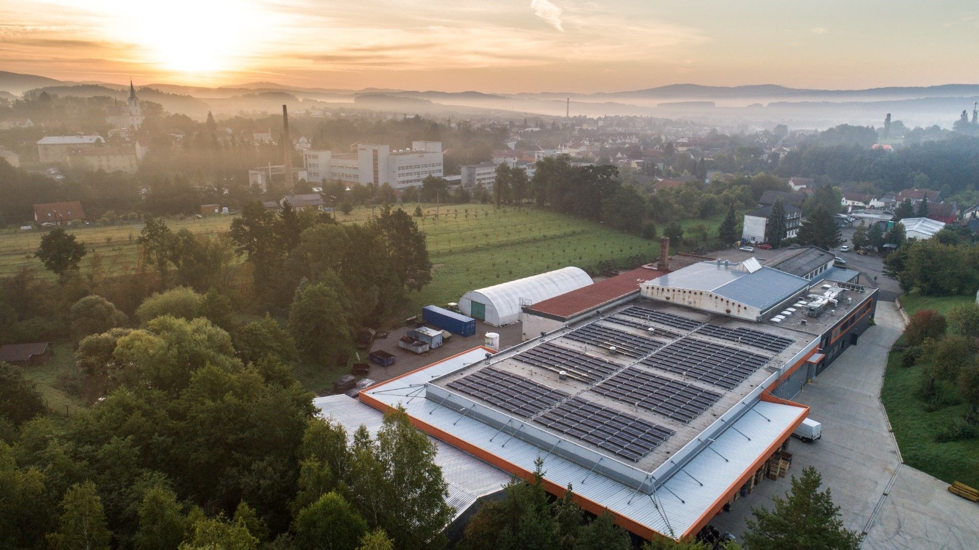 Aerial view of a factory with solar panels on the roof at sunrise.