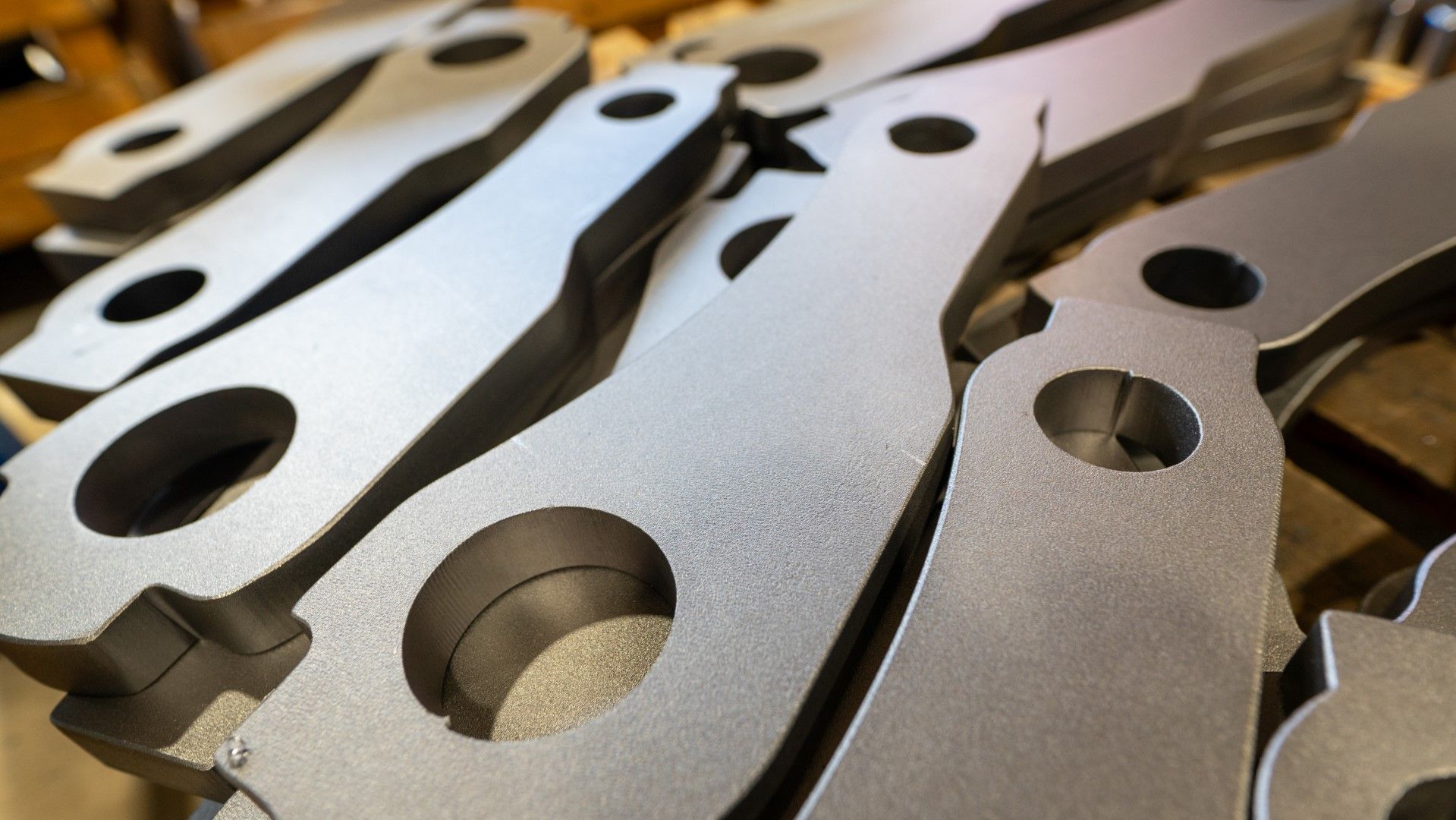 A pile of identical, metallic components with circular holes.