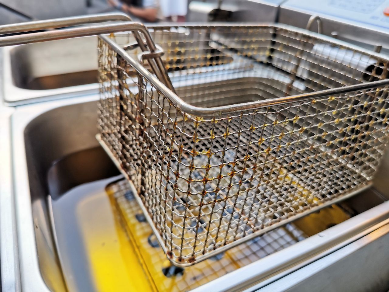 A metal deep fryer basket is partially submerged in bubbling hot oil.