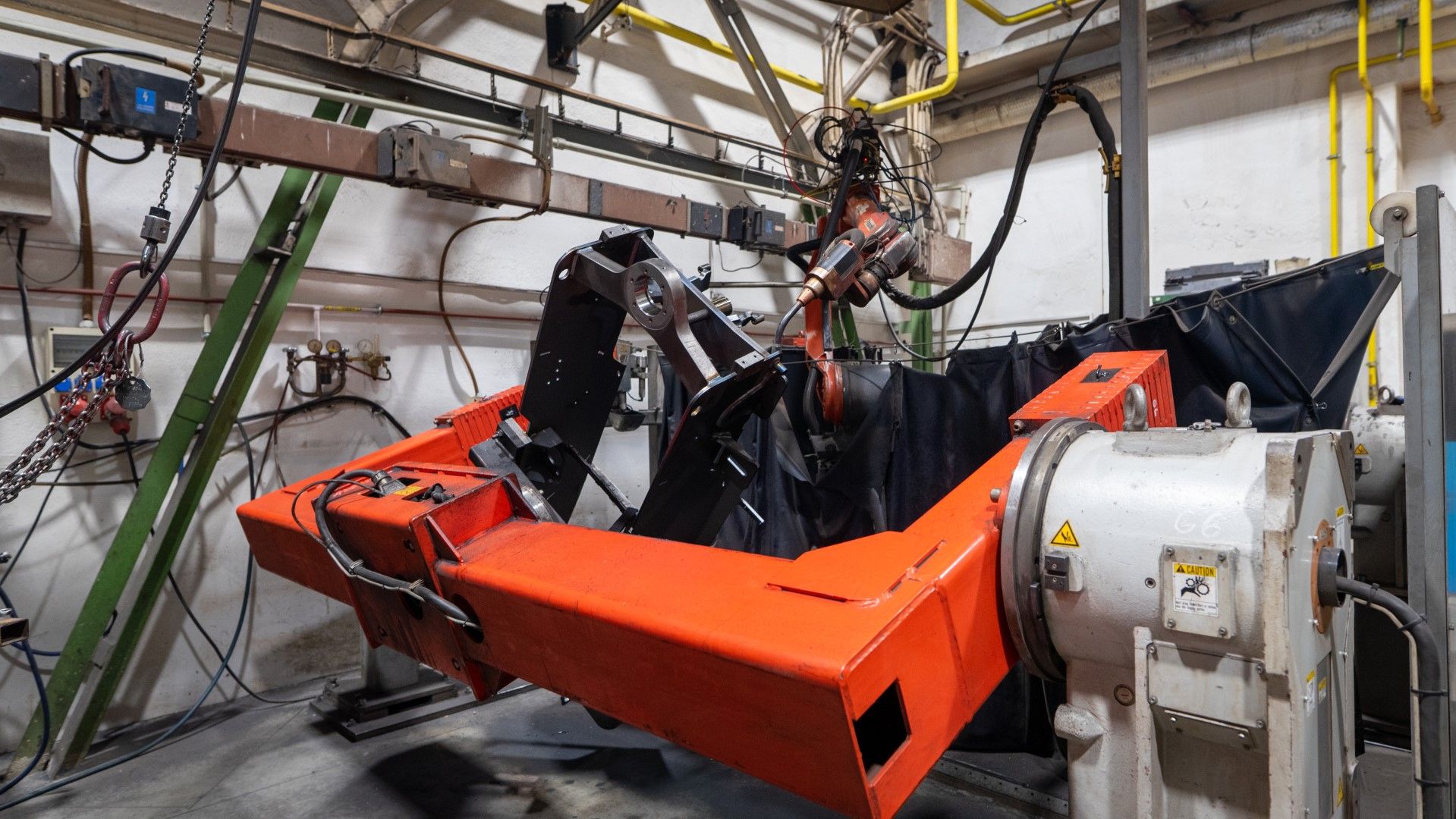 Robotic arm with orange and black components manipulates black fabric in a manufacturing setting.