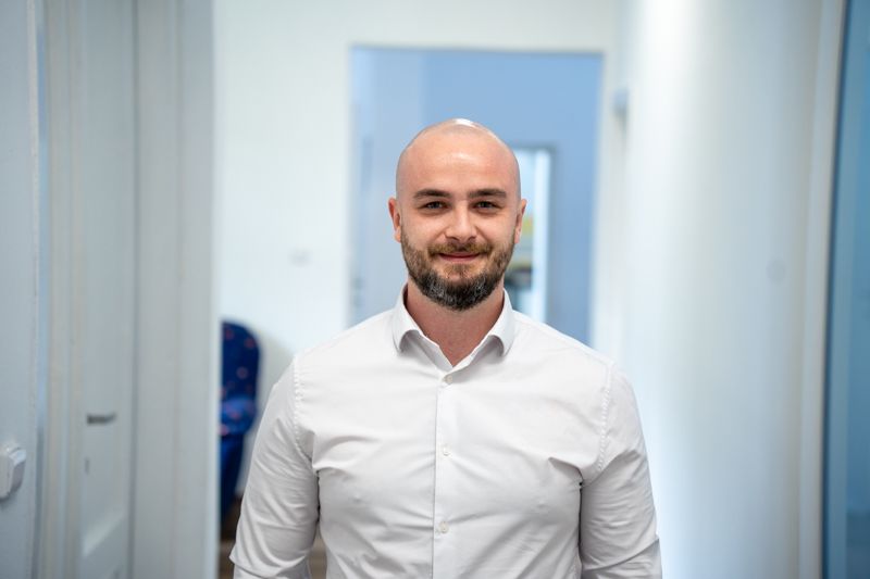 Smiling man with bald head and beard wearing white button-up shirt.
