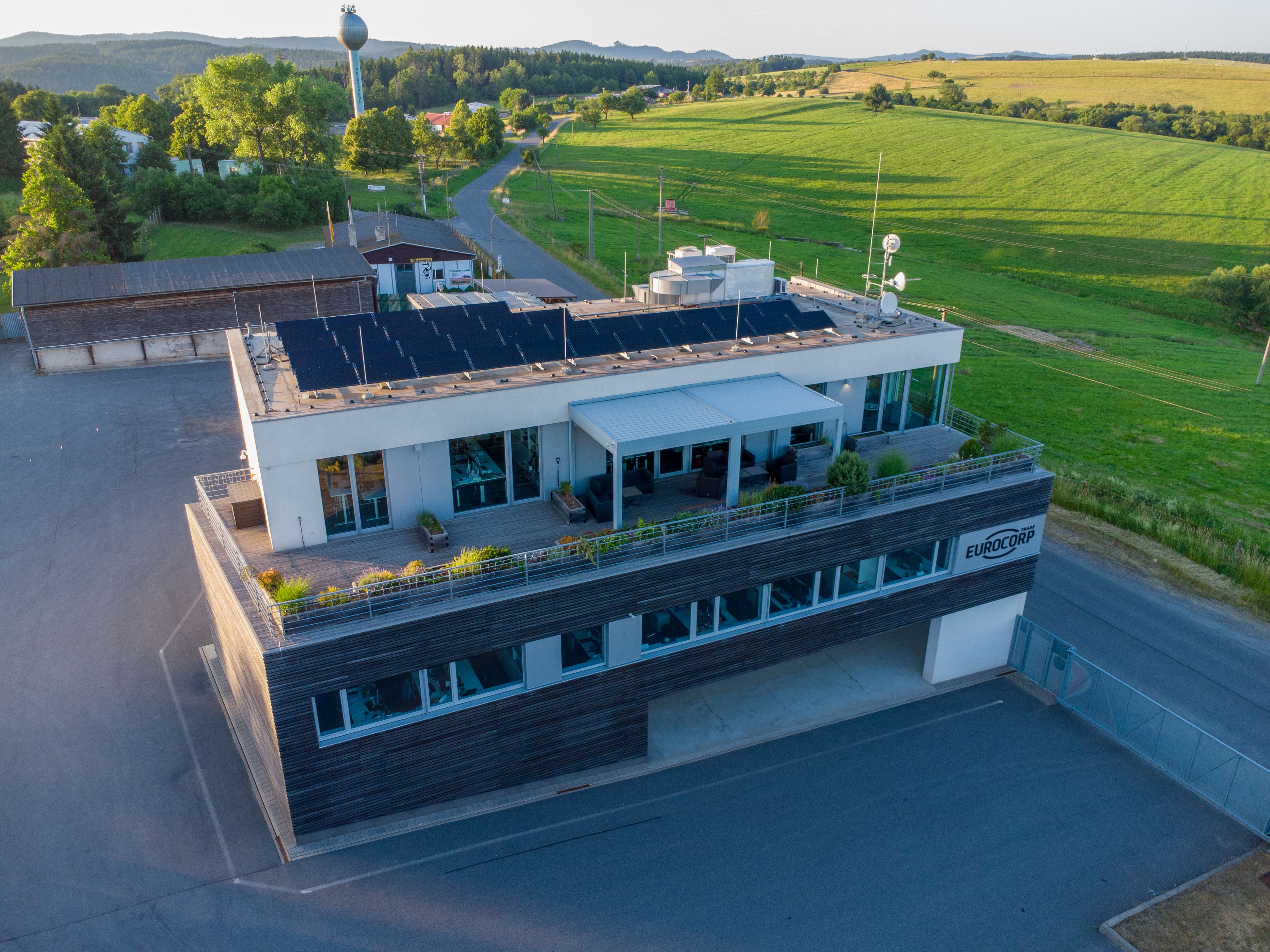 Modern building with rooftop solar panels and a green terrace in a rural landscape.