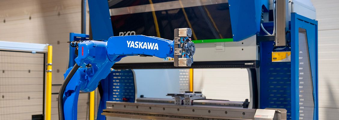 Blue Yaskawa robotic arm positioned in front of industrial manufacturing machinery.